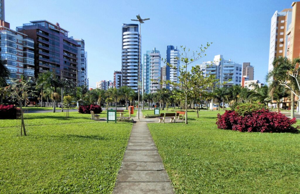 Vibrant urban park with skyscrapers in the background, lush greenery and clear blue sky.